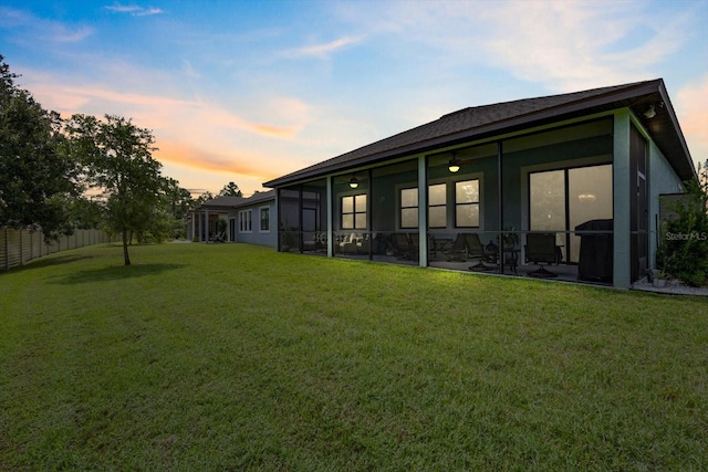 back house at dusk with a sunroom and a yard