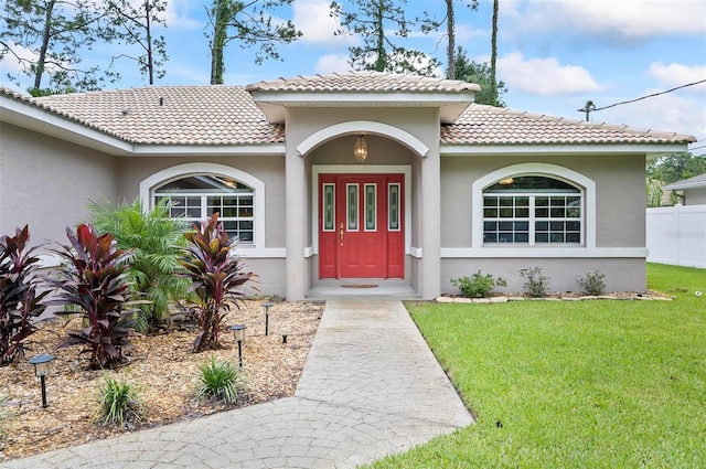 entrance to property with a tile roof, a yard, and stucco siding