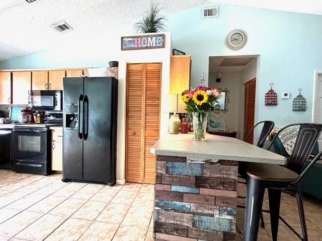 kitchen with a textured ceiling, lofted ceiling, a kitchen bar, black appliances, and light tile patterned floors