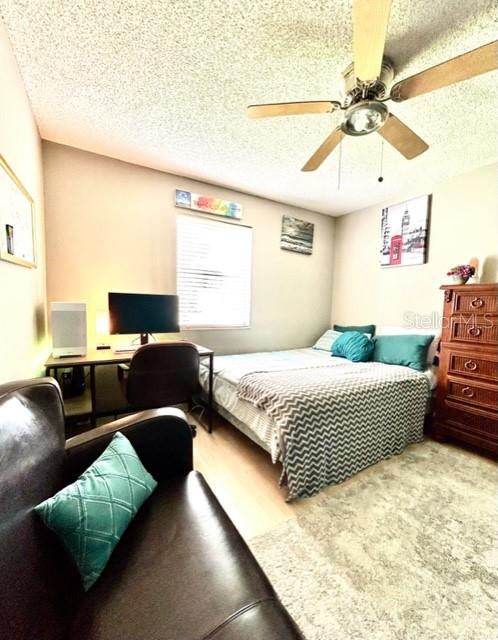 carpeted bedroom featuring ceiling fan and a textured ceiling