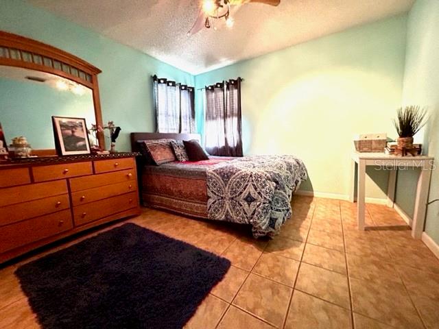 tiled bedroom with ceiling fan and a textured ceiling