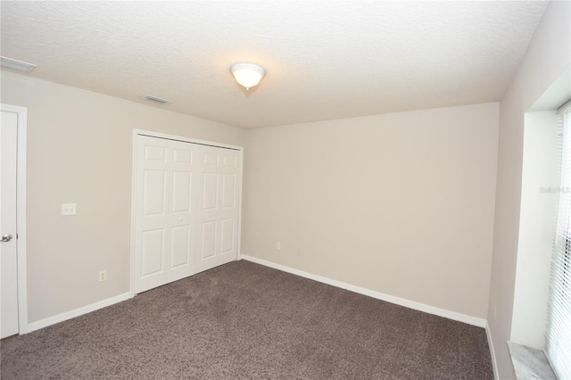 unfurnished bedroom featuring a textured ceiling, dark colored carpet, and a closet