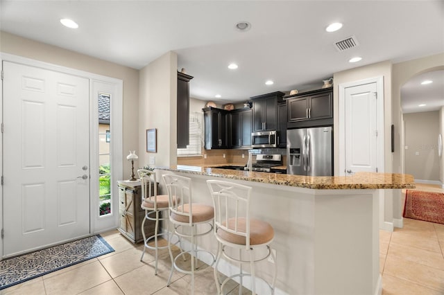 kitchen featuring a kitchen breakfast bar, stainless steel appliances, backsplash, light tile patterned floors, and light stone counters