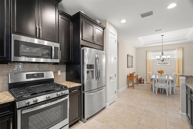 kitchen featuring tasteful backsplash, a raised ceiling, appliances with stainless steel finishes, light stone countertops, and a chandelier