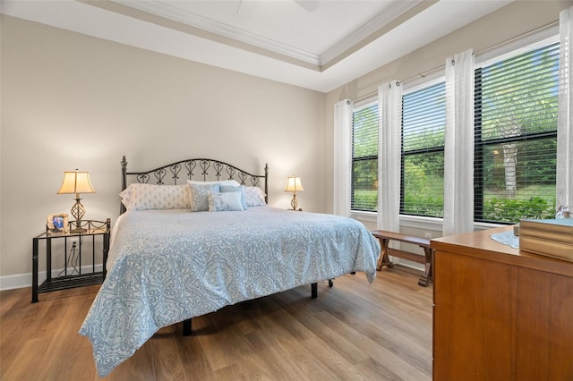 bedroom featuring light hardwood / wood-style flooring, ceiling fan, a raised ceiling, and crown molding