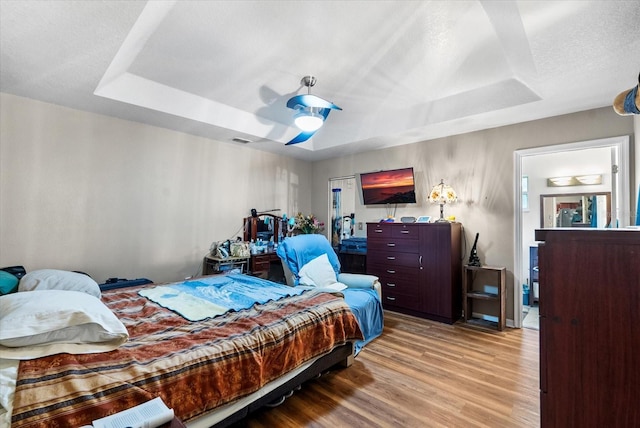 bedroom with ceiling fan, light hardwood / wood-style floors, and a raised ceiling