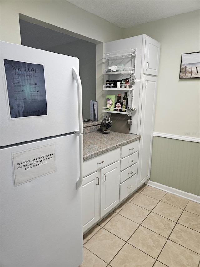 kitchen with a textured ceiling, light tile patterned floors, white cabinets, and white fridge