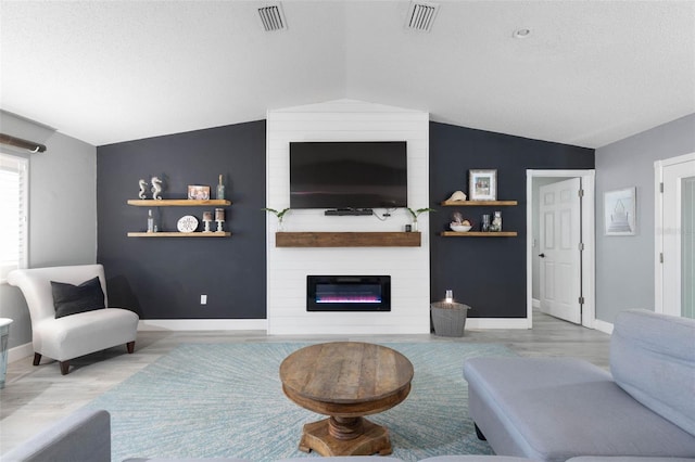 living room with a textured ceiling, light hardwood / wood-style flooring, vaulted ceiling, and a large fireplace