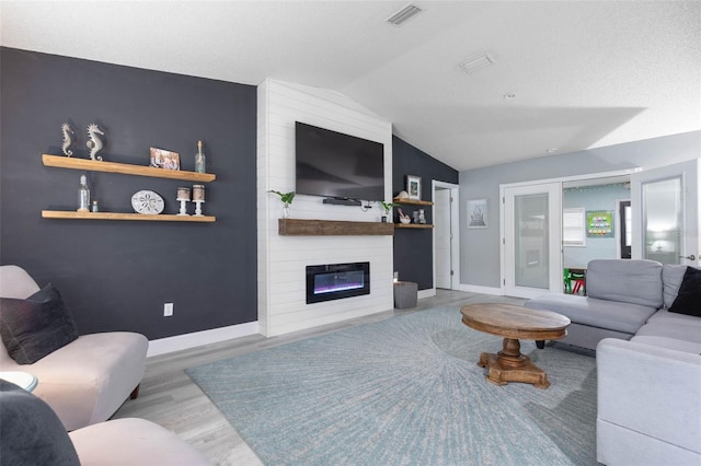 living room with light wood-type flooring, a textured ceiling, lofted ceiling, and a large fireplace