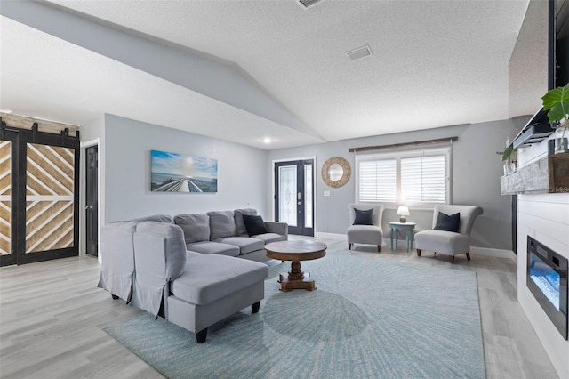 living room with light hardwood / wood-style flooring, vaulted ceiling, and a textured ceiling