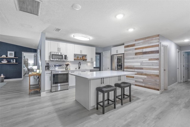 kitchen with light hardwood / wood-style floors, white cabinetry, stainless steel appliances, a textured ceiling, and lofted ceiling