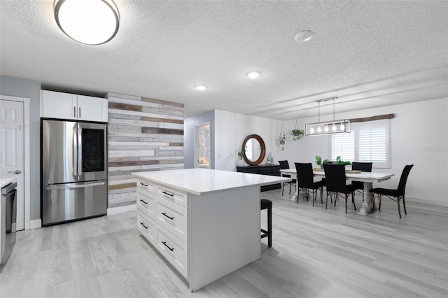 kitchen featuring hanging light fixtures, stainless steel fridge, a kitchen island, white cabinetry, and light hardwood / wood-style floors