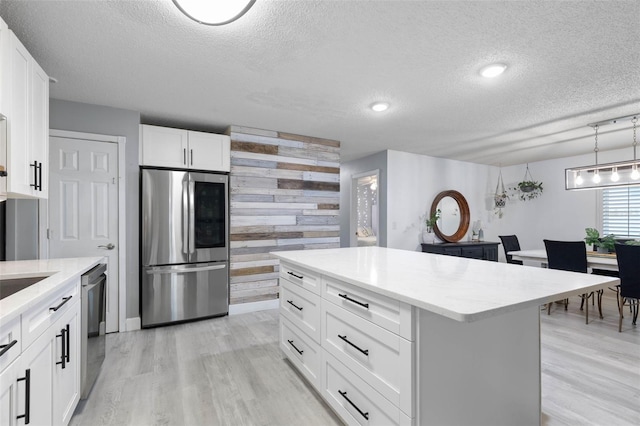 kitchen featuring a textured ceiling, stainless steel appliances, a center island, and white cabinetry