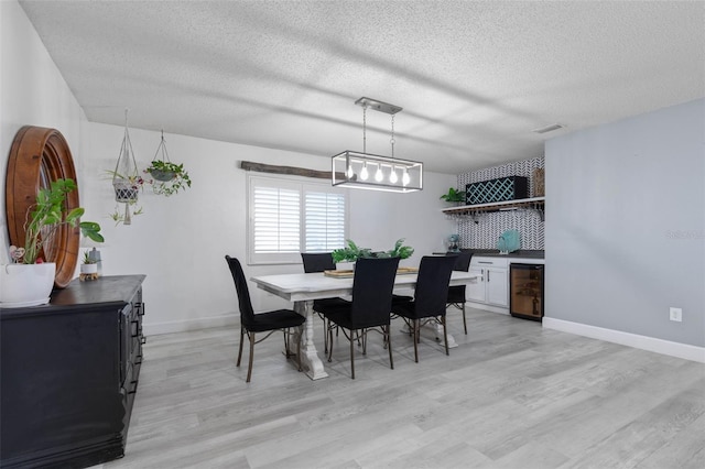 dining room with a textured ceiling, light hardwood / wood-style floors, and wine cooler