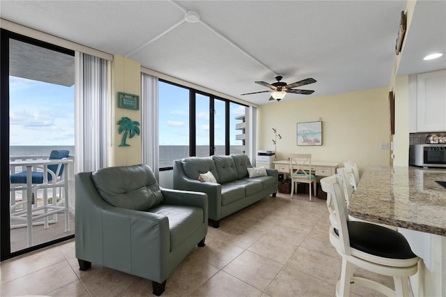 living room featuring a water view, expansive windows, light tile patterned floors, and ceiling fan