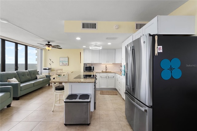 kitchen with a breakfast bar area, stone countertops, appliances with stainless steel finishes, white cabinetry, and ceiling fan