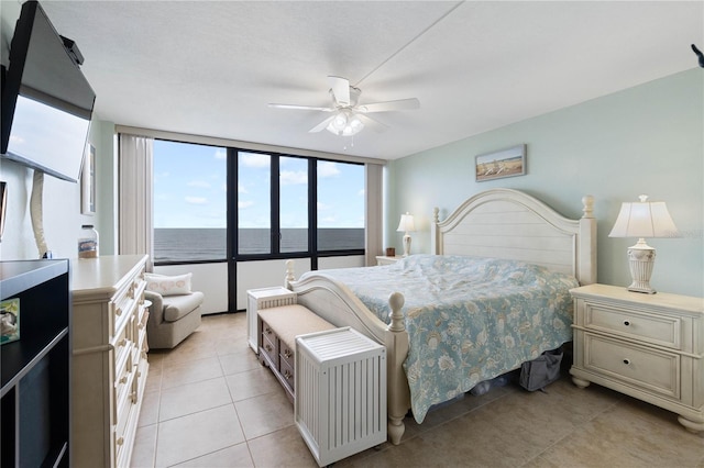 bedroom with a water view, ceiling fan, light tile patterned floors, and expansive windows