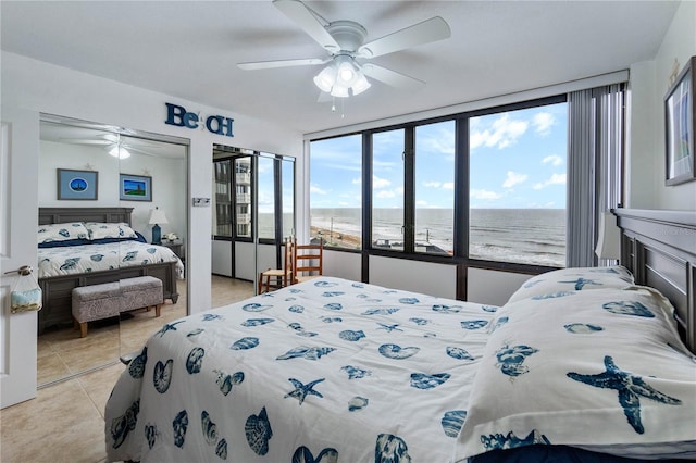 tiled bedroom featuring a view of the beach, a water view, ceiling fan, and a closet