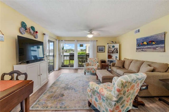 living room featuring light wood-type flooring, ceiling fan, and a textured ceiling