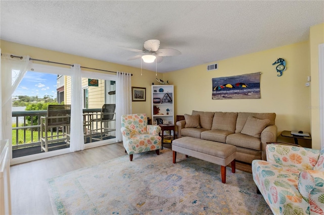 living room with a textured ceiling, ceiling fan, and light wood-type flooring