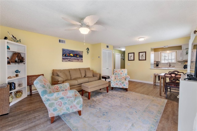 living room with ceiling fan, hardwood / wood-style flooring, a textured ceiling, and sink