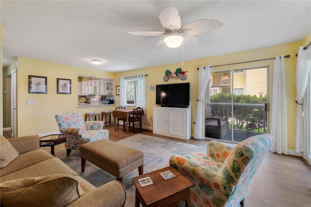 living room with ceiling fan, light hardwood / wood-style floors, and a textured ceiling