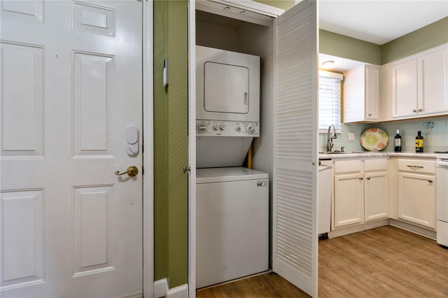 laundry area featuring stacked washing maching and dryer, light hardwood / wood-style floors, and sink