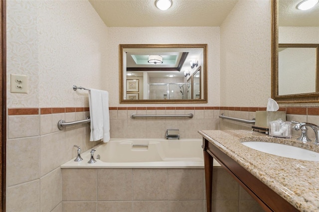 bathroom with plus walk in shower, tile walls, a textured ceiling, and vanity