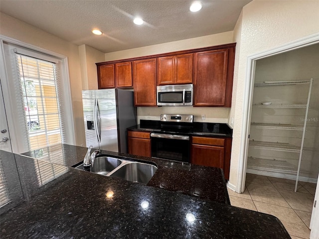 kitchen with dark stone countertops, light tile patterned flooring, stainless steel appliances, a textured ceiling, and sink