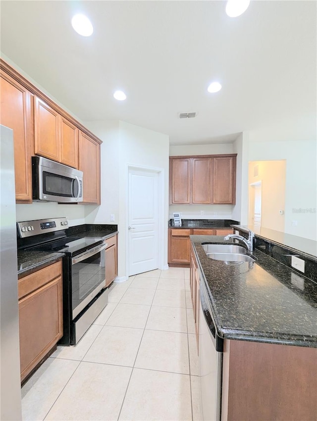 kitchen featuring dark stone countertops, light tile patterned flooring, appliances with stainless steel finishes, and sink