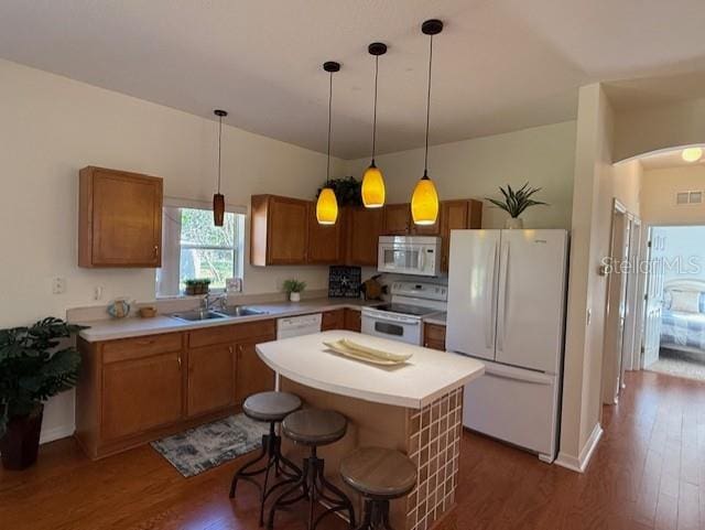 kitchen featuring a breakfast bar, white appliances, dark wood-type flooring, decorative light fixtures, and a center island