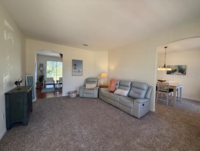 living room featuring dark colored carpet and ceiling fan with notable chandelier