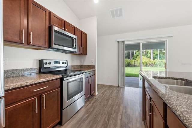 kitchen with appliances with stainless steel finishes, dark stone counters, vaulted ceiling, and light hardwood / wood-style flooring