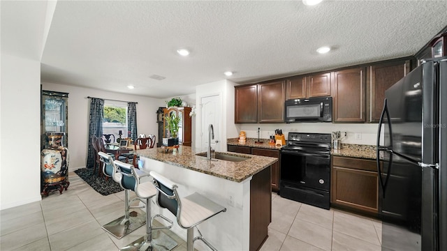 kitchen with black appliances, a kitchen island with sink, sink, and light stone counters