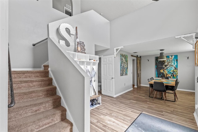 staircase with a barn door, a towering ceiling, and hardwood / wood-style floors