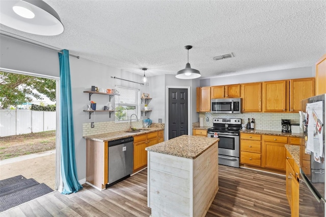 kitchen with hanging light fixtures, sink, a kitchen island, wood-type flooring, and appliances with stainless steel finishes