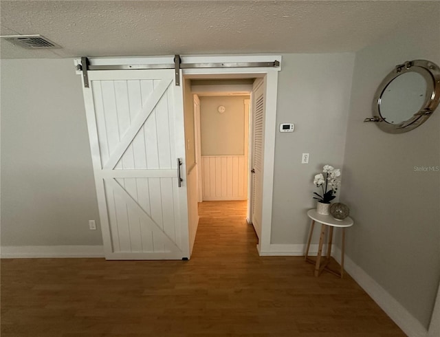 hall with a barn door, a textured ceiling, and hardwood / wood-style flooring