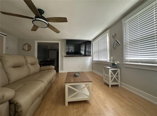 living room with a textured ceiling, ceiling fan, and light hardwood / wood-style flooring