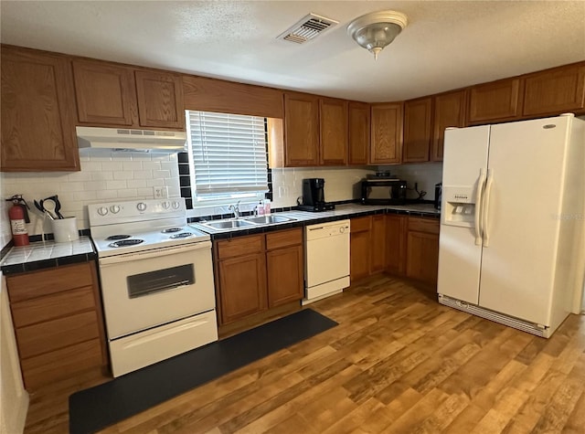 kitchen featuring sink, light hardwood / wood-style flooring, white appliances, backsplash, and tile countertops