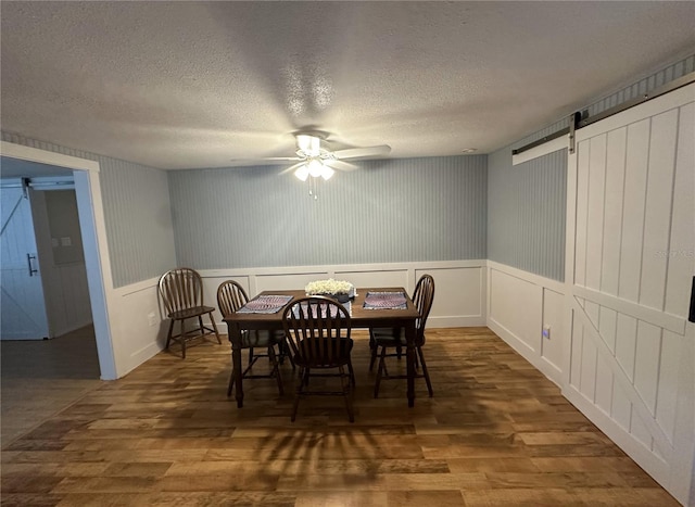 dining area with ceiling fan, a textured ceiling, a barn door, and dark hardwood / wood-style flooring