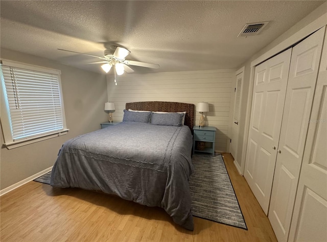 bedroom with ceiling fan, a textured ceiling, wood walls, and light hardwood / wood-style floors