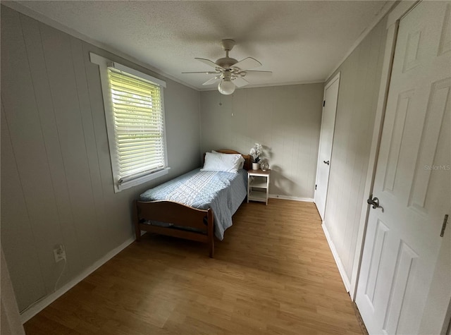 bedroom with ceiling fan, ornamental molding, wooden walls, and light hardwood / wood-style floors