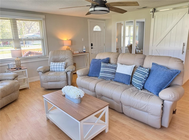 living room with a barn door, visible vents, ceiling fan, a textured ceiling, and light wood-type flooring