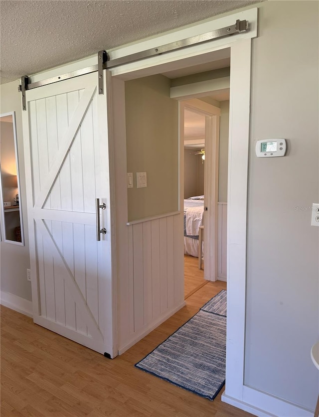 interior space with a textured ceiling, a barn door, wainscoting, and light wood-style floors