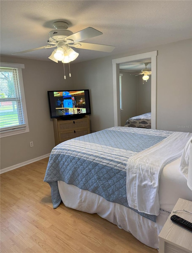 bedroom with ceiling fan, a textured ceiling, baseboards, and wood finished floors