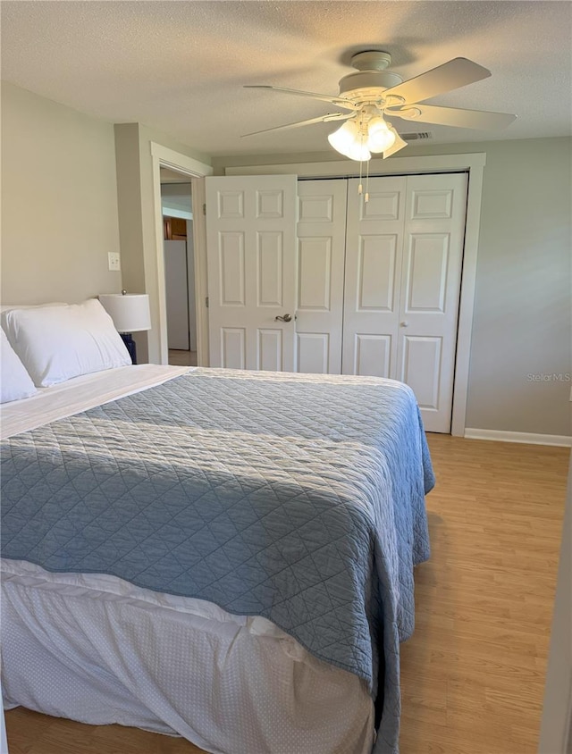 bedroom featuring baseboards, light wood-style flooring, ceiling fan, a textured ceiling, and a closet