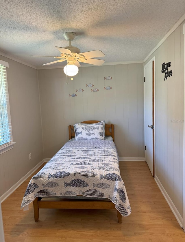 bedroom with a textured ceiling, ornamental molding, light wood-type flooring, and a ceiling fan