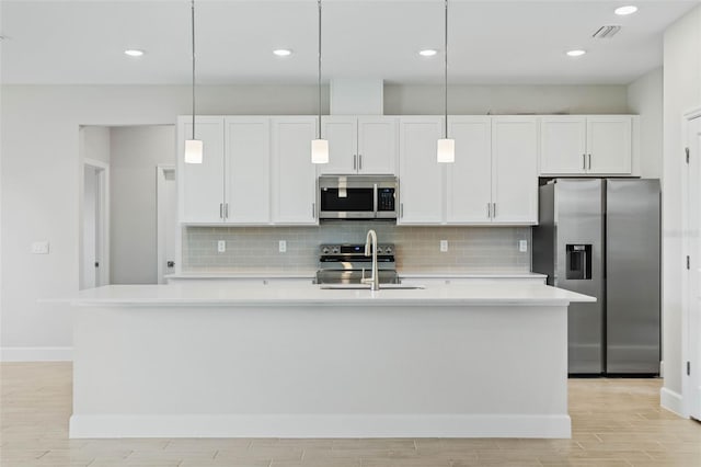 kitchen featuring white cabinets, a center island with sink, appliances with stainless steel finishes, and light hardwood / wood-style flooring