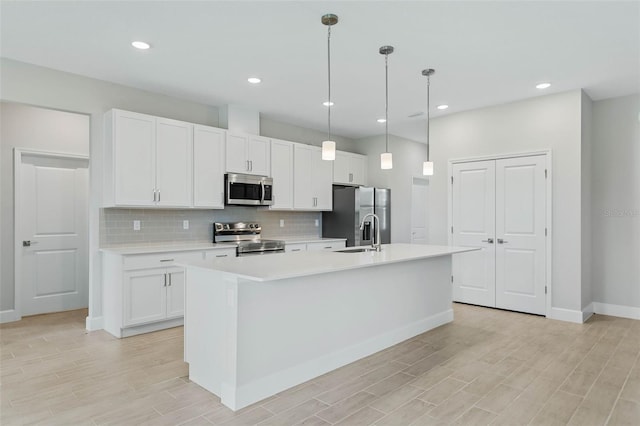 kitchen with light wood-type flooring, an island with sink, white cabinets, decorative backsplash, and appliances with stainless steel finishes