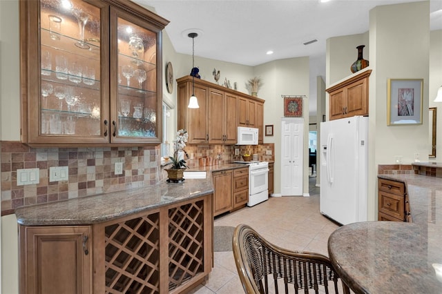 kitchen featuring white appliances, dark stone countertops, light tile patterned flooring, and hanging light fixtures